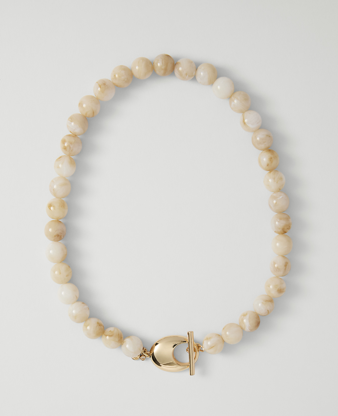 A necklace of pale, marbled beads with a gold clasp rests on a plain white background.