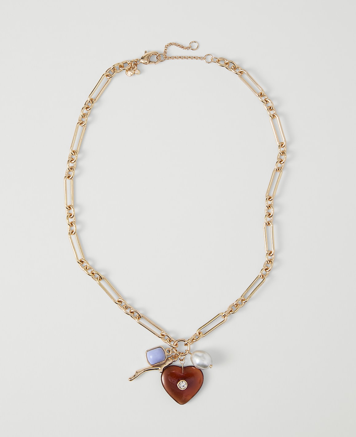 A gold chain necklace with a heart-shaped pendant and charms rests on a plain white background.