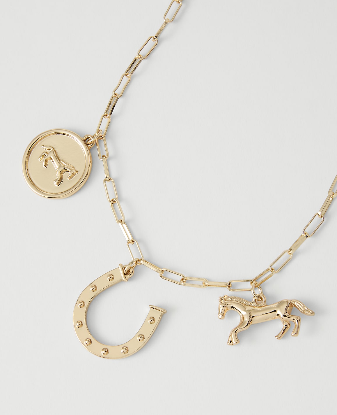 A gold necklace with horse and horseshoe charms rests on a plain white background.