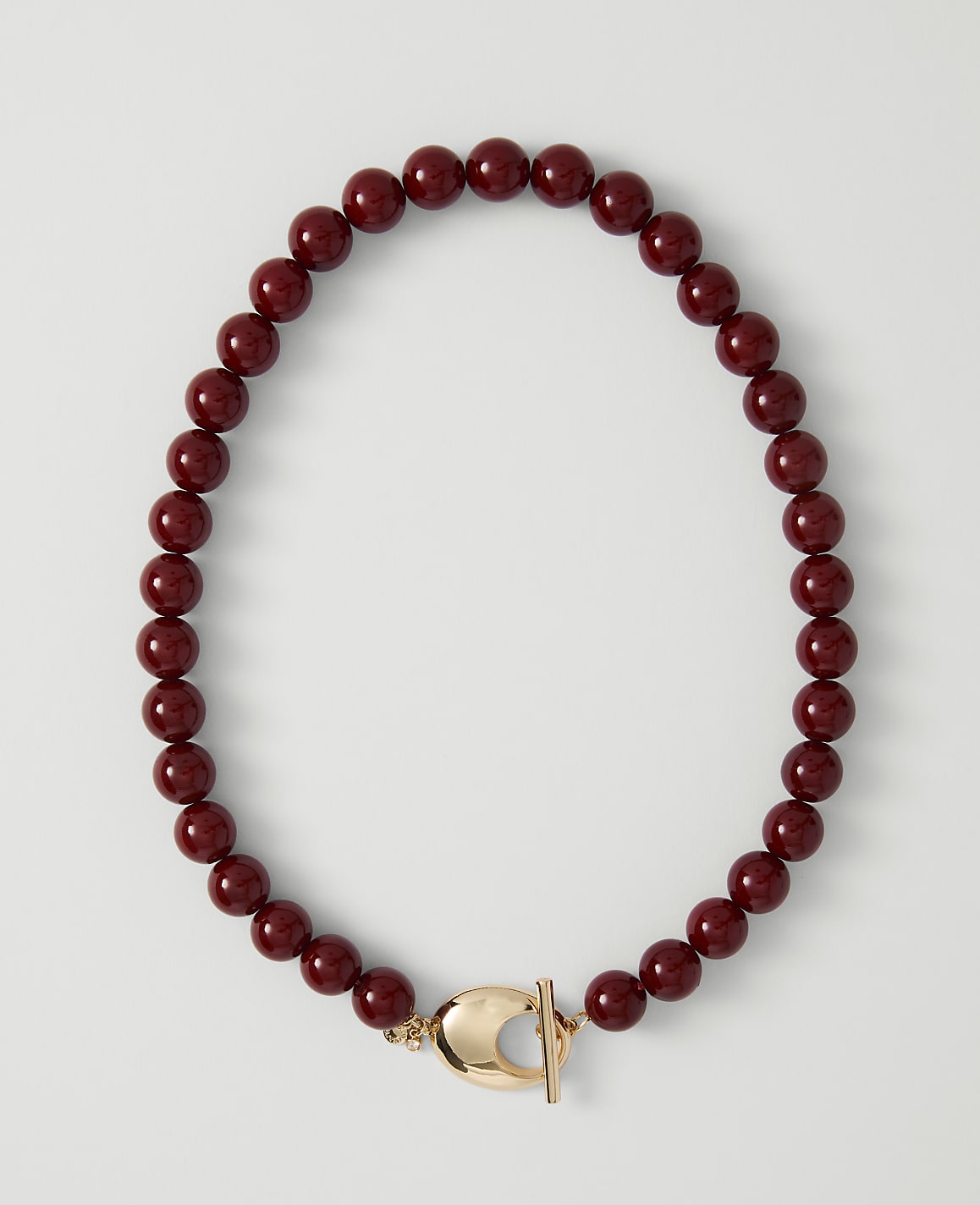 A deep red beaded necklace with a gold clasp lies on a plain white background.