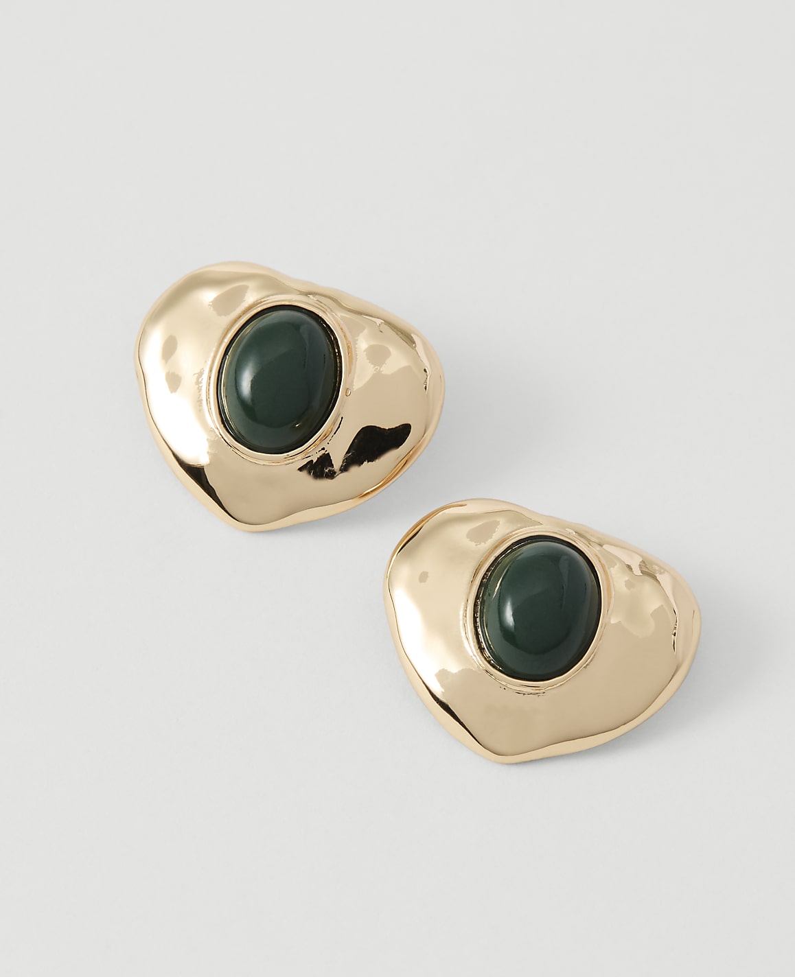 Two gold, heart-shaped earrings with dark green stones are displayed against a plain white background.