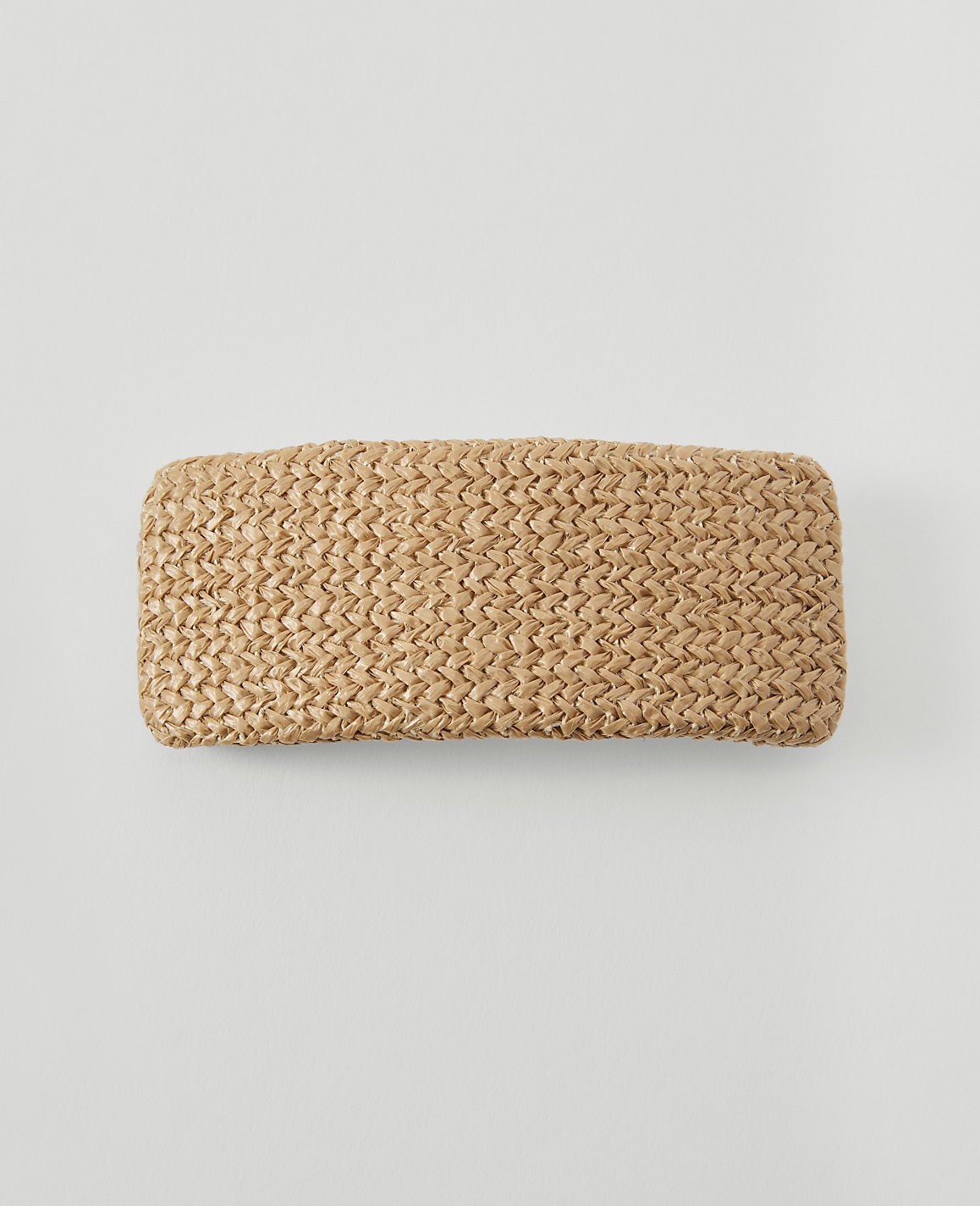 A woven straw clutch rests on a plain, light gray background.