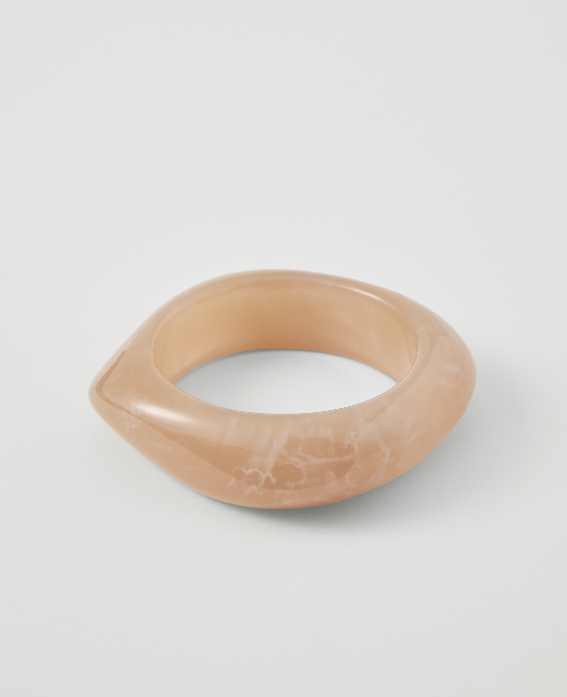 A translucent, peachy-pink bangle with a marbled pattern rests on a plain white background.