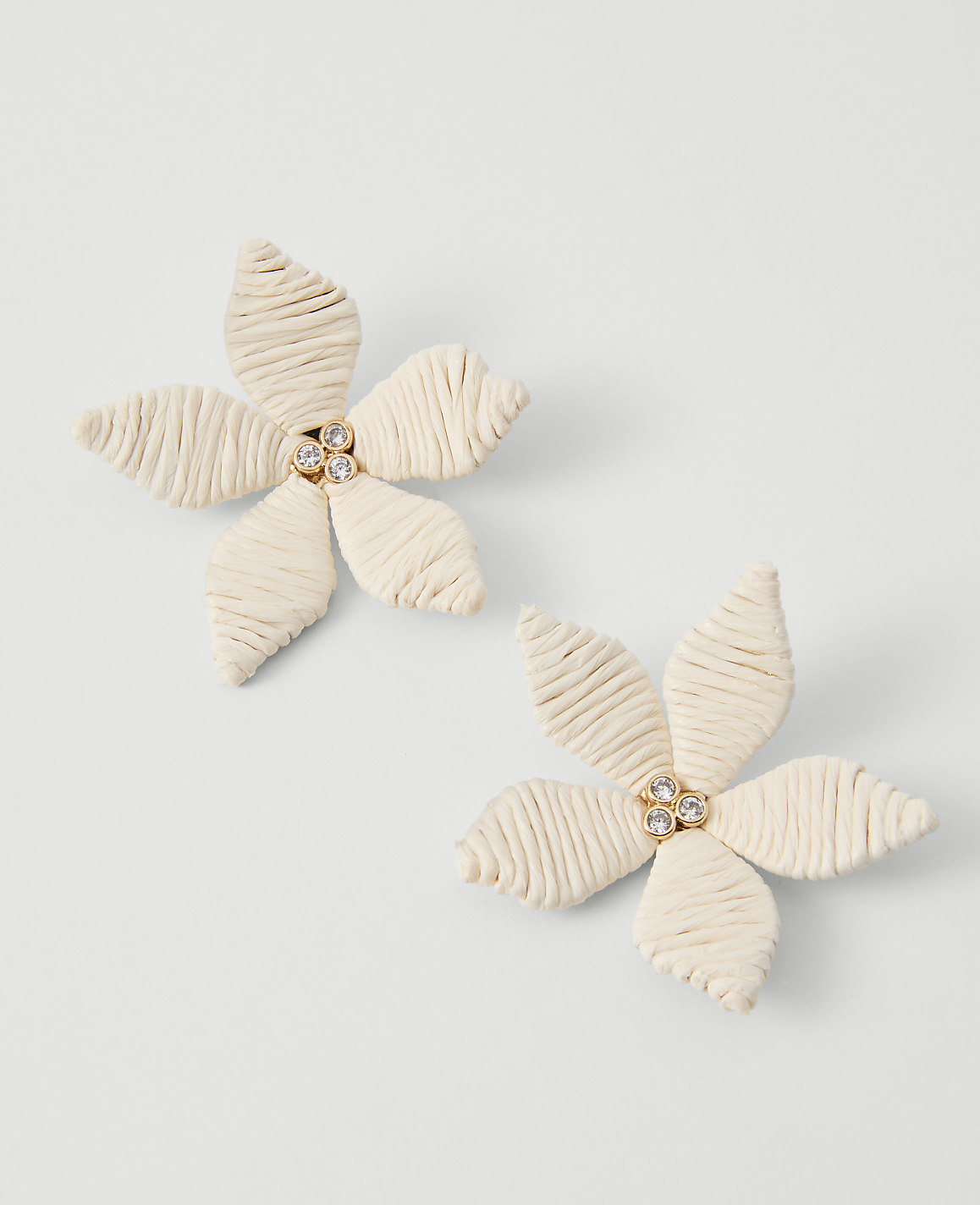 Two cream-colored floral earrings with rhinestone centers rest on a plain white background.