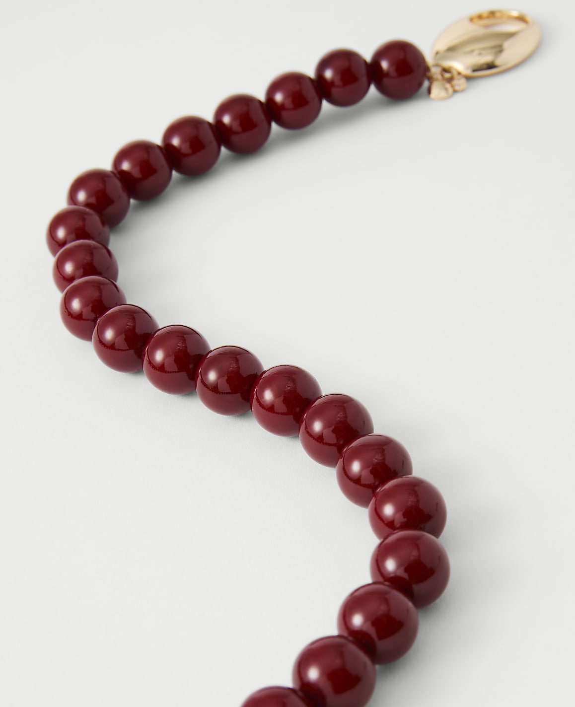 A strand of deep red beads curves across a pale background, culminating in a gold clasp.