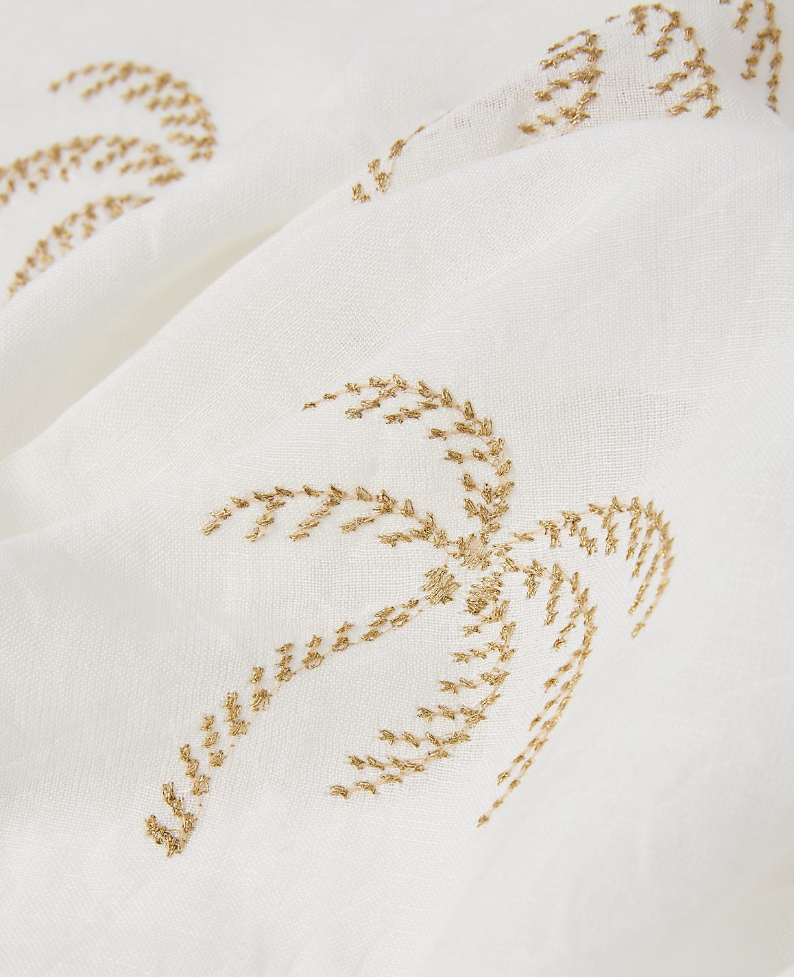 A close-up of a white fabric with embroidered golden palm trees in the foreground and background.
