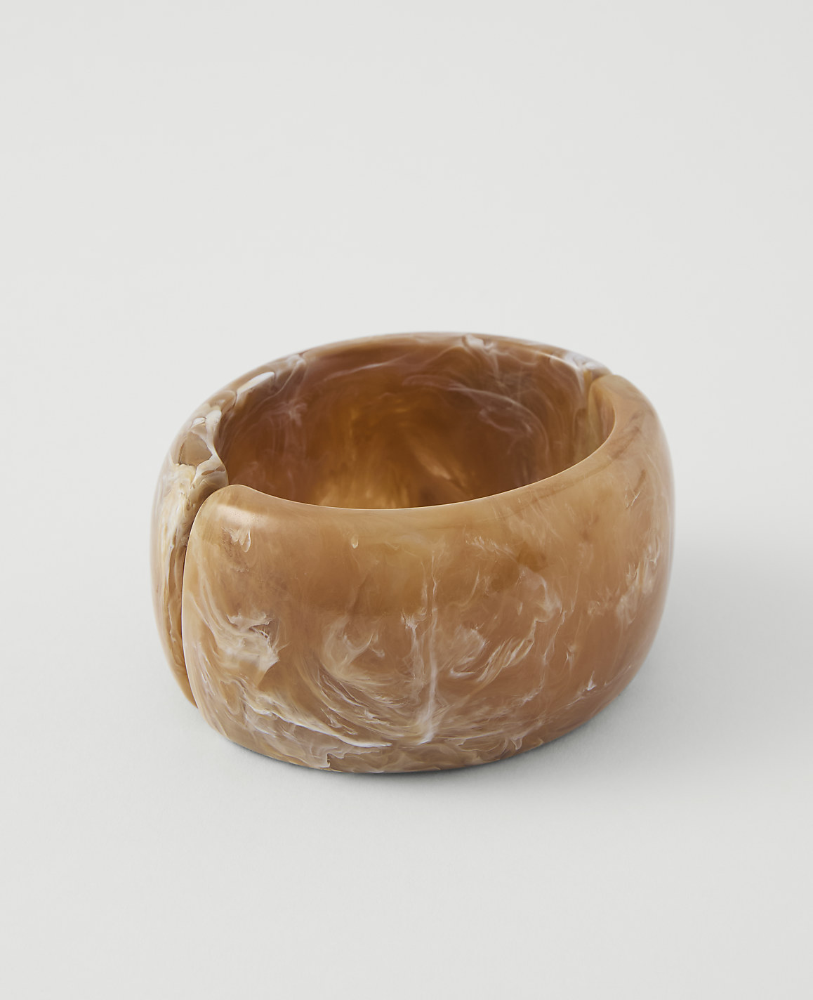 A chunky, marbled tan and white resin bangle rests on a plain white background.
