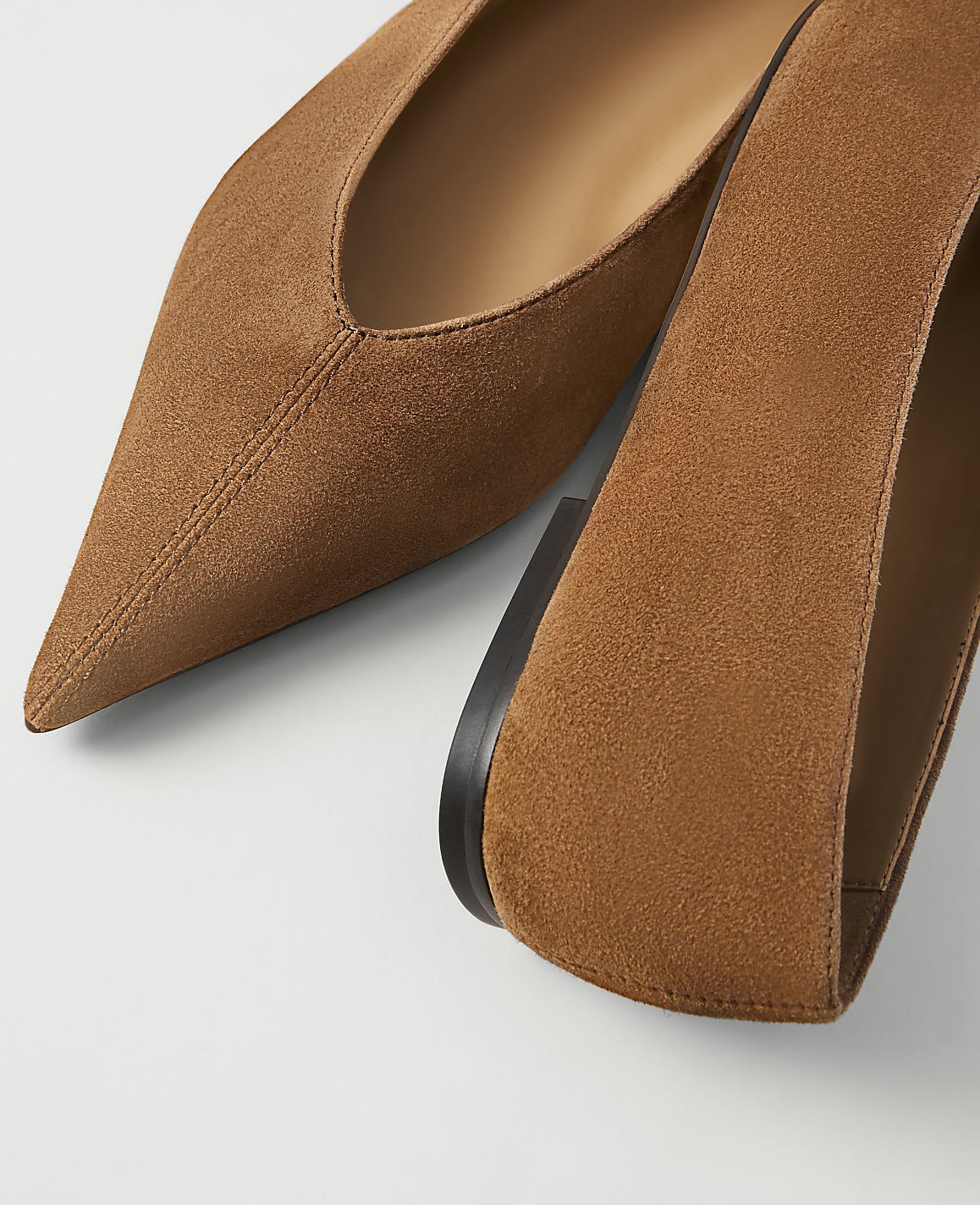 A pair of brown suede pointed-toe flats are shown against a white background.