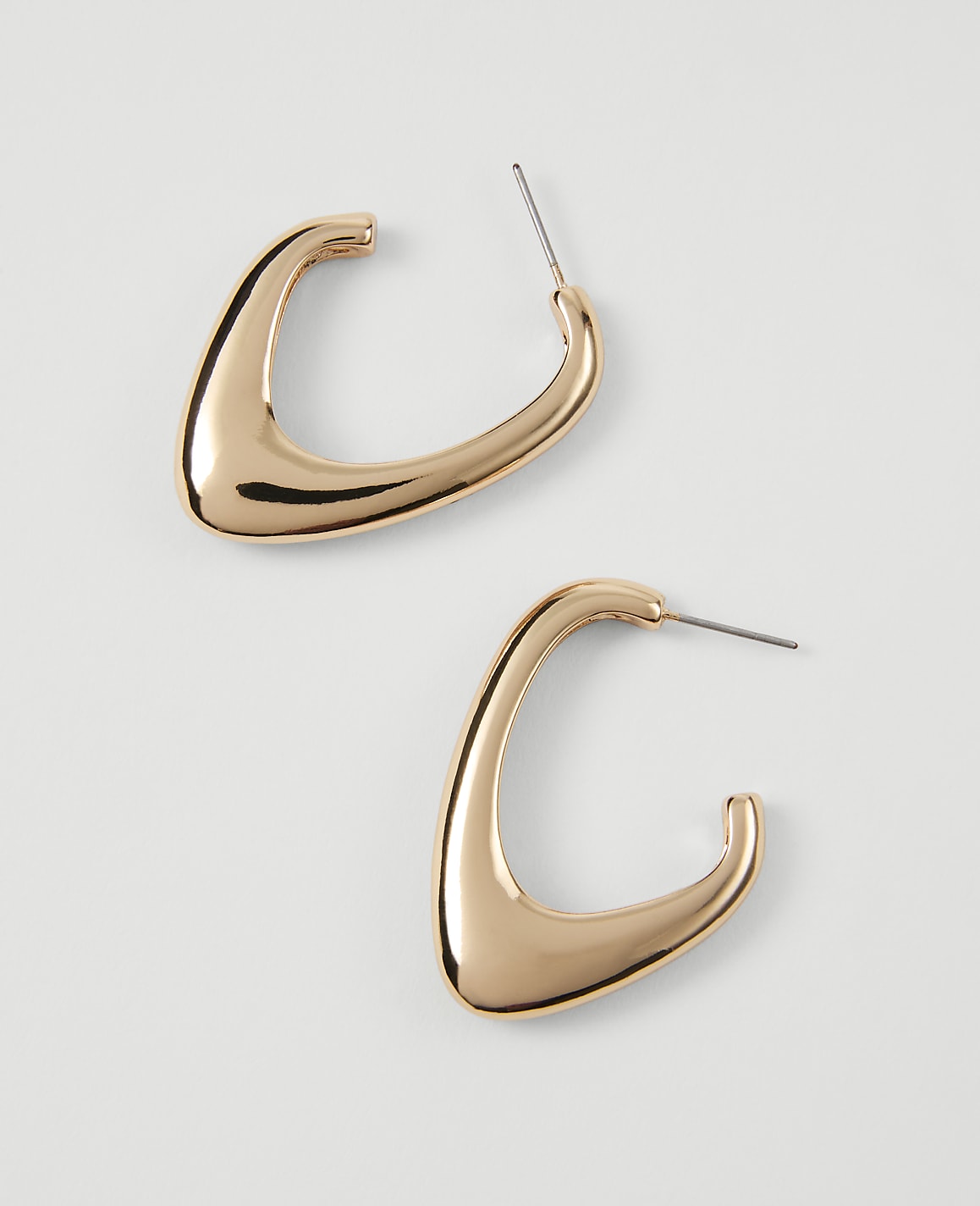 Two polished gold abstract hoop earrings rest on a plain white background.