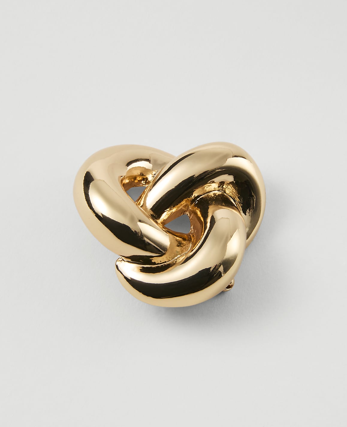 A shiny gold knot rests on a plain white background.