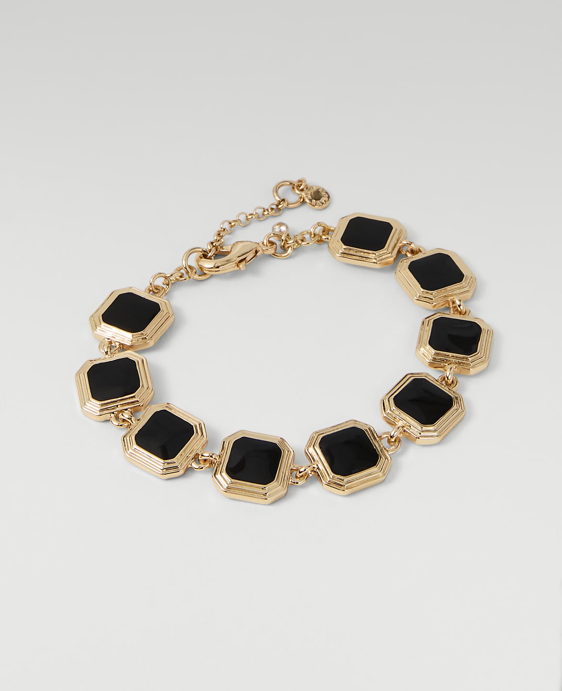 A gold bracelet with black square stones is displayed against a plain white background.