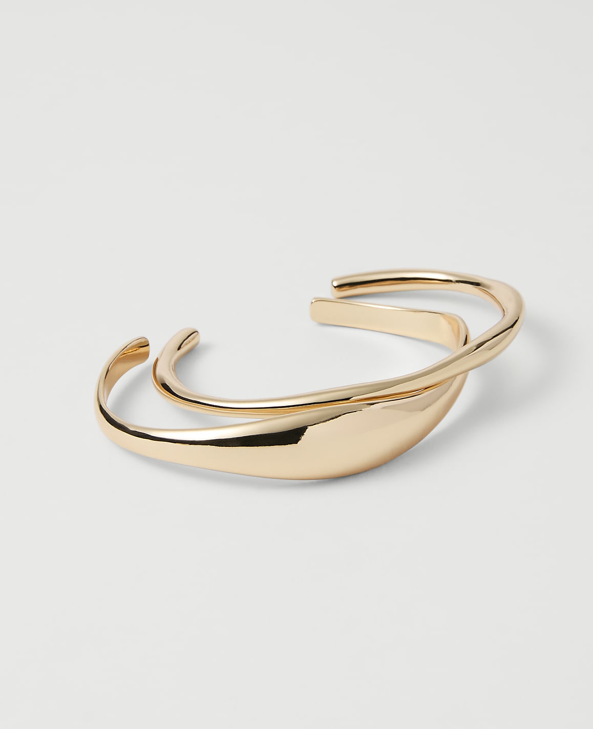 A pair of intertwined gold bangles rests on a plain white background.