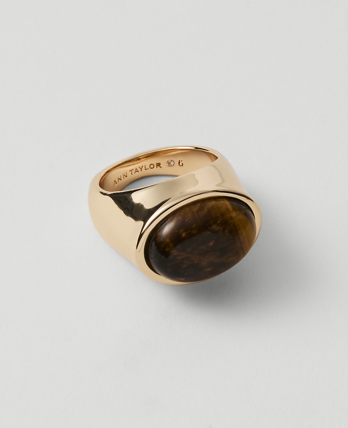 A gold ring with a tiger's eye stone sits on a plain white background.