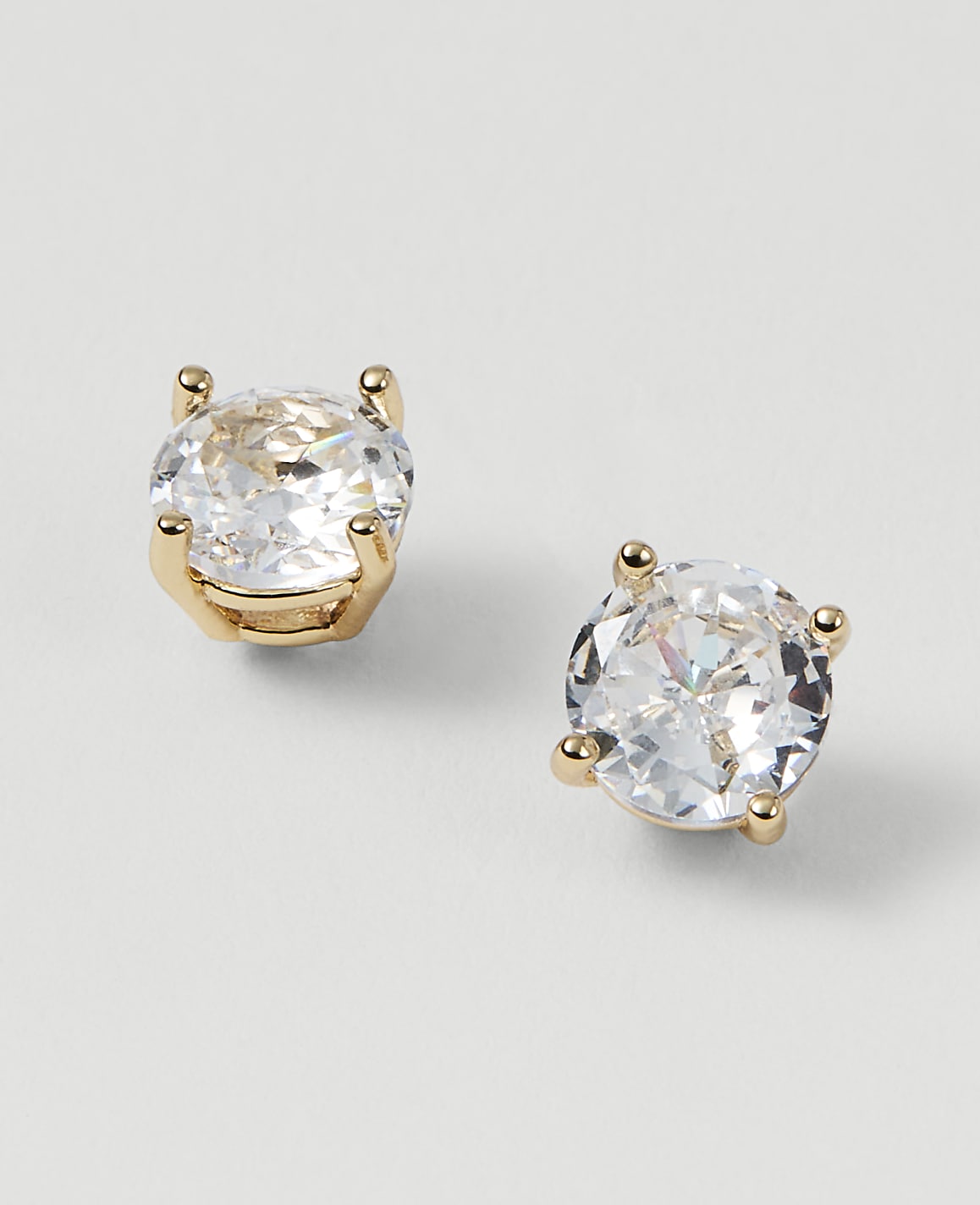 Two sparkling diamond stud earrings with gold settings rest on a plain white background.