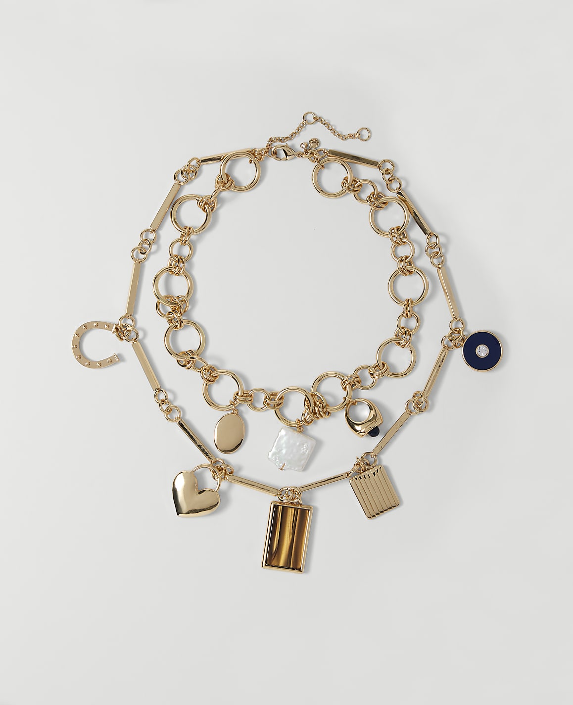 Two gold necklaces with various charms, including a heart, horseshoe, and geometric shapes, are laid out on a plain white background.