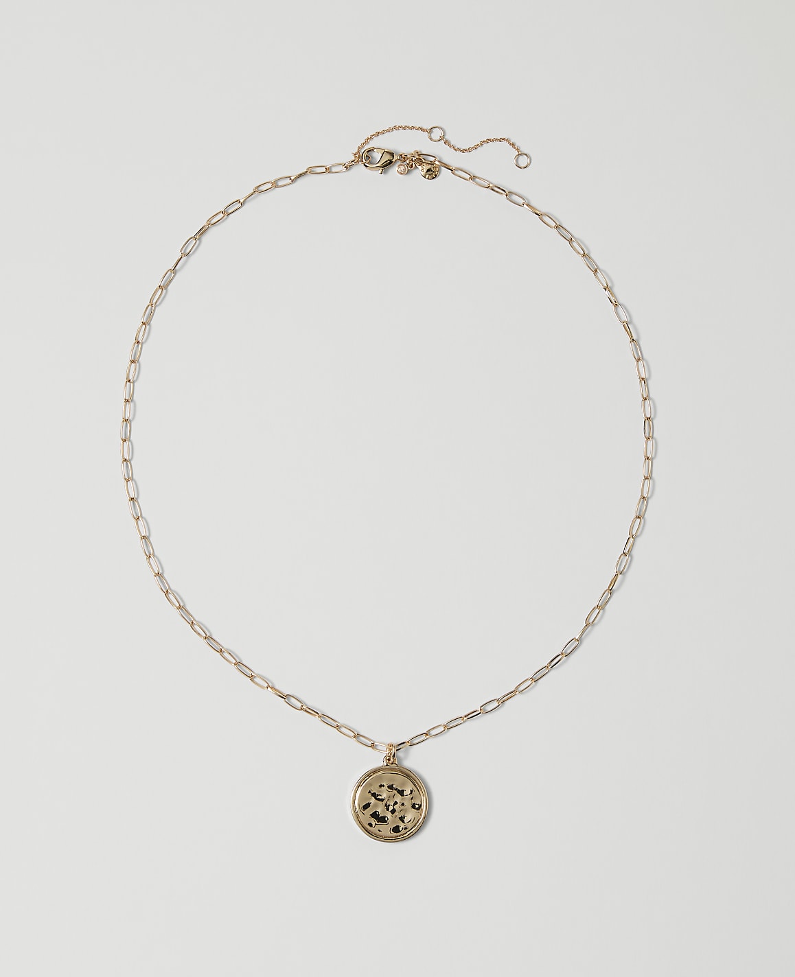 A delicate gold chain necklace with a circular pendant rests on a plain white background.