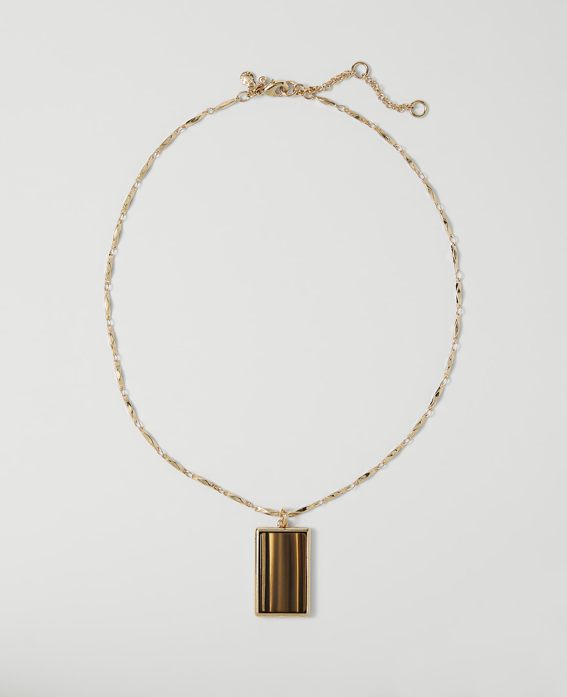 A gold necklace with a rectangular tiger's eye pendant rests on a plain white background.
