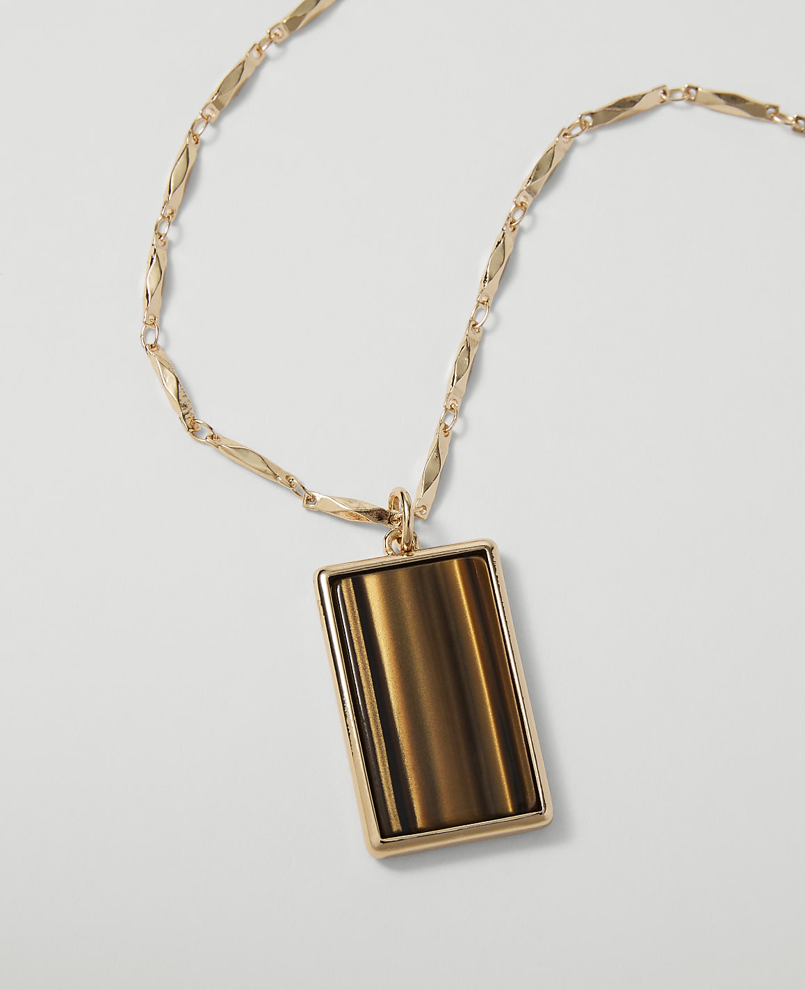 A rectangular tiger's eye pendant hangs from a delicate gold chain against a plain white background.