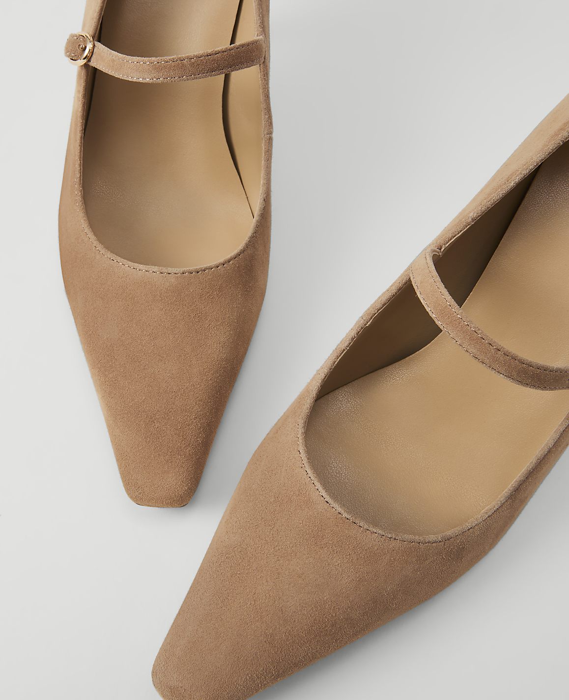 Two tan suede Mary Jane heels with thin ankle straps are arranged on a white background.
