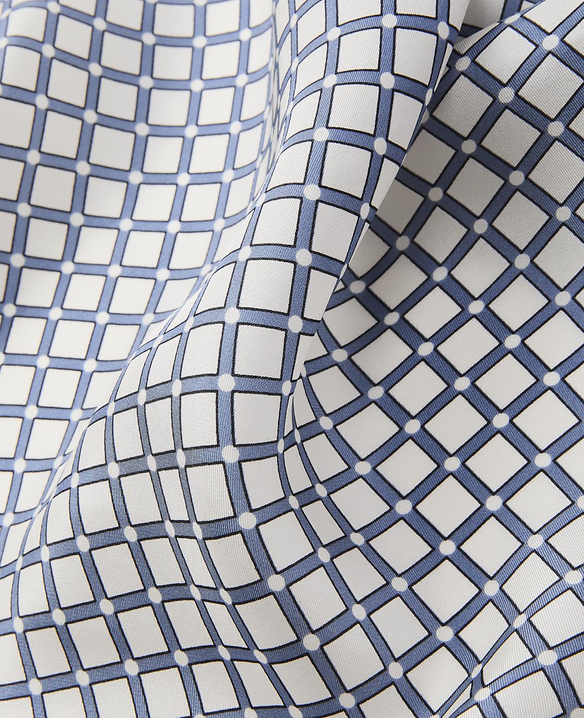 A close-up of white fabric with a repeating pattern of blue squares and white dots creates a textured foreground against a softly folded background of the same material.