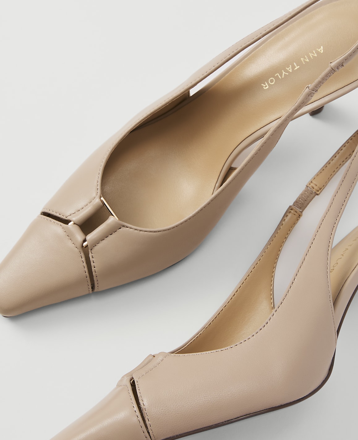 Two nude slingback heels with pointed toes and gold accents are displayed against a plain white background.