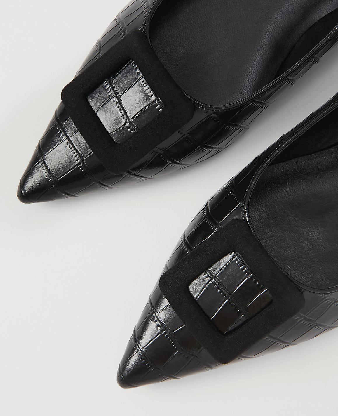 Two black, pointed-toe heels with croc-embossed texture and a square black buckle are laid out on a white background.