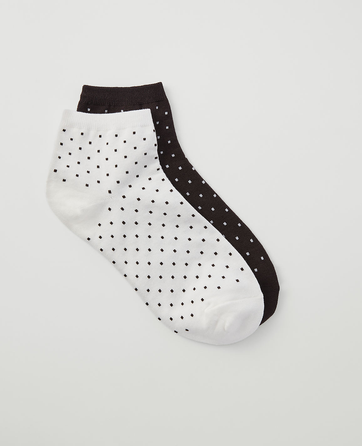 A pair of white and dark brown polka dot ankle socks lie on a plain white background.