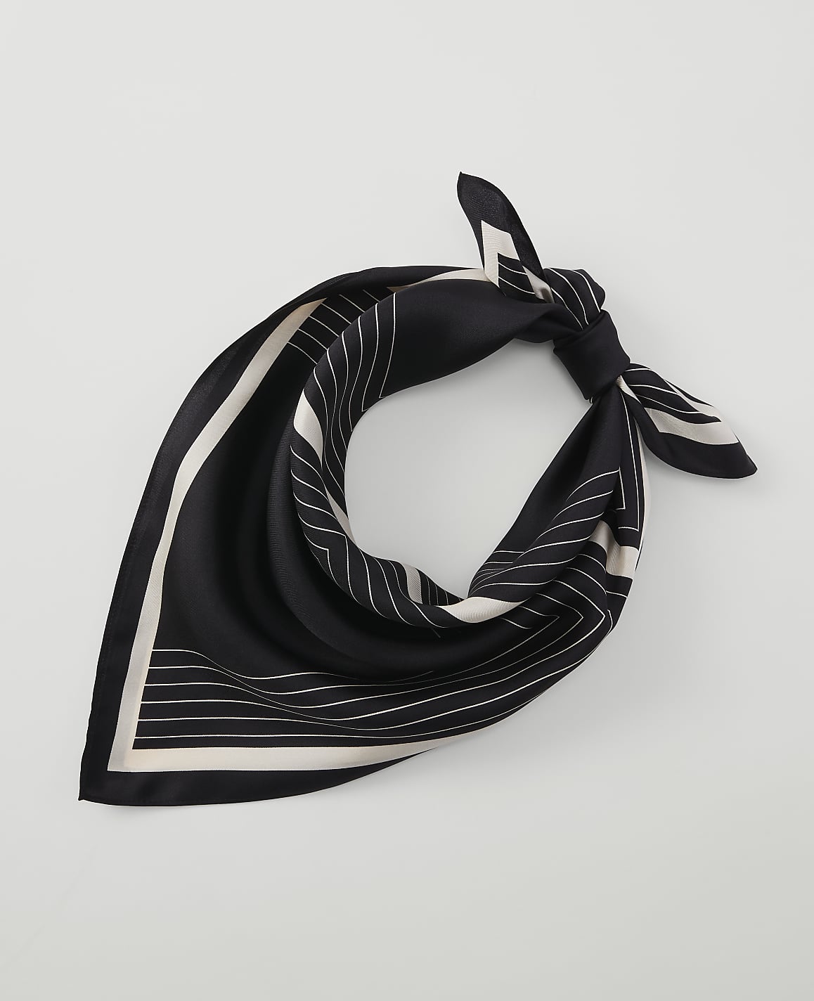 A black silk scarf with white geometric lines is tied in a knot against a plain white background.