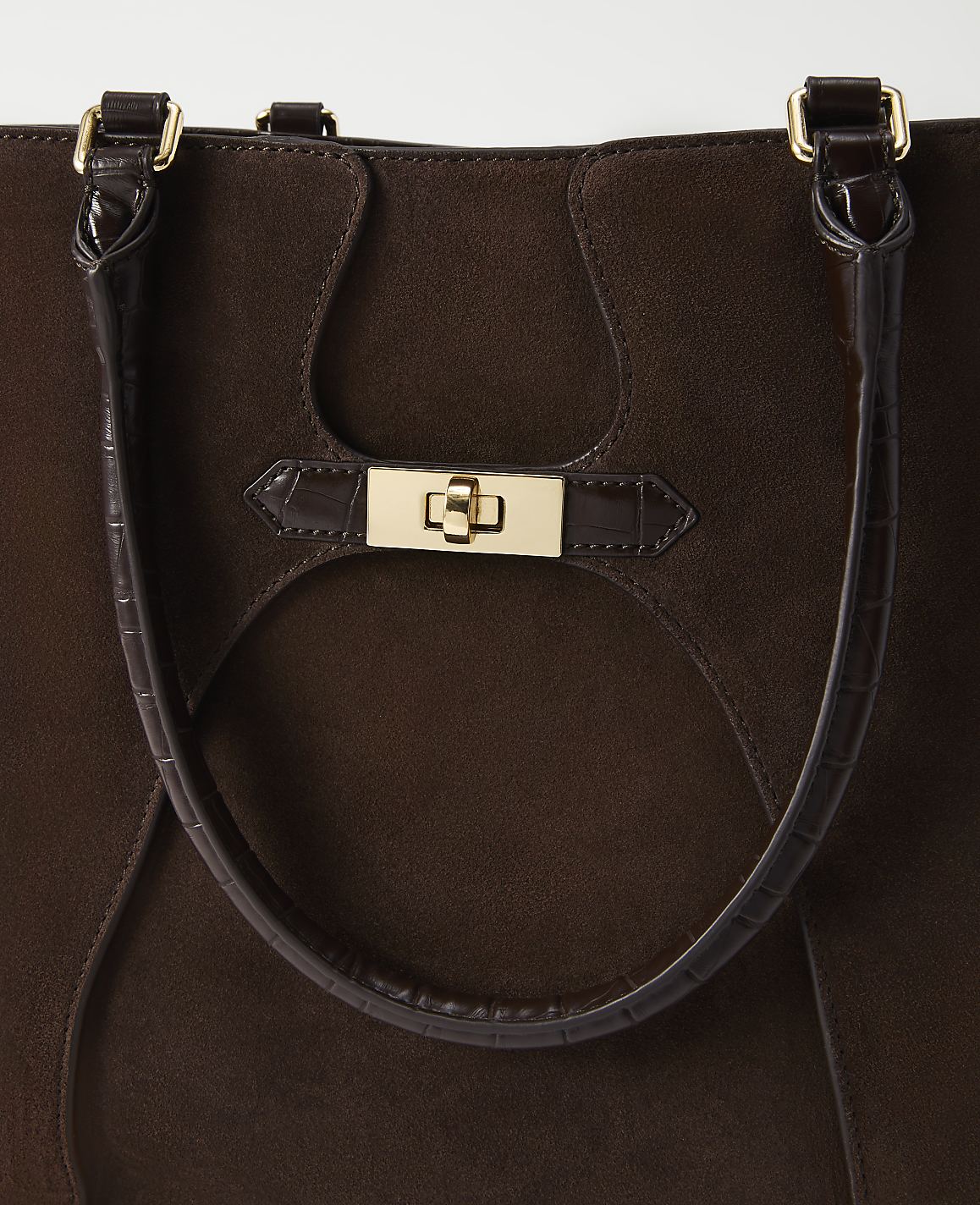 A close-up of a dark brown suede tote bag with a gold clasp and croc-embossed leather accents is presented against a plain white background.
