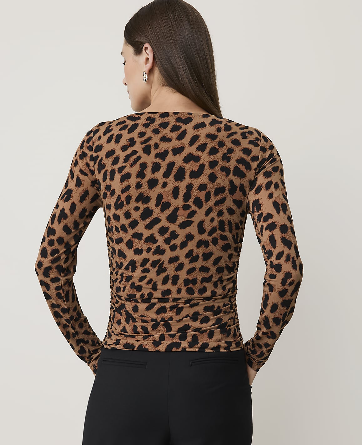 A woman in a leopard print top and black pants stands against a plain, light-colored background.
