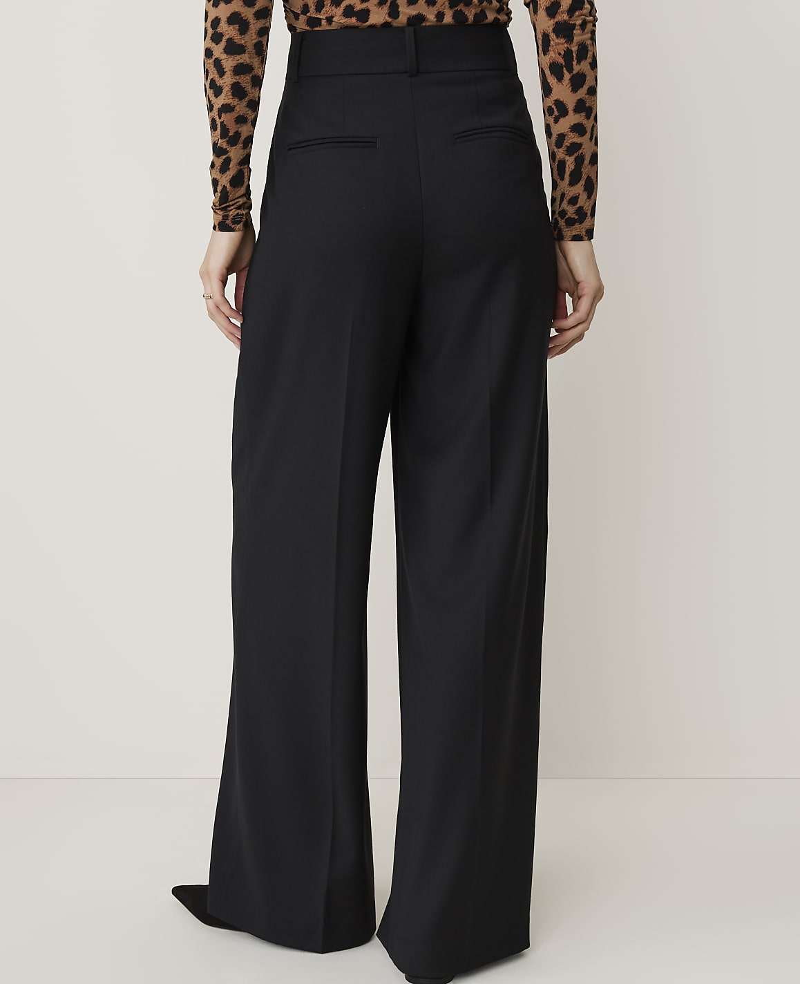 A person wearing black wide-leg pants and a leopard-print top stands against a plain, light-colored background.