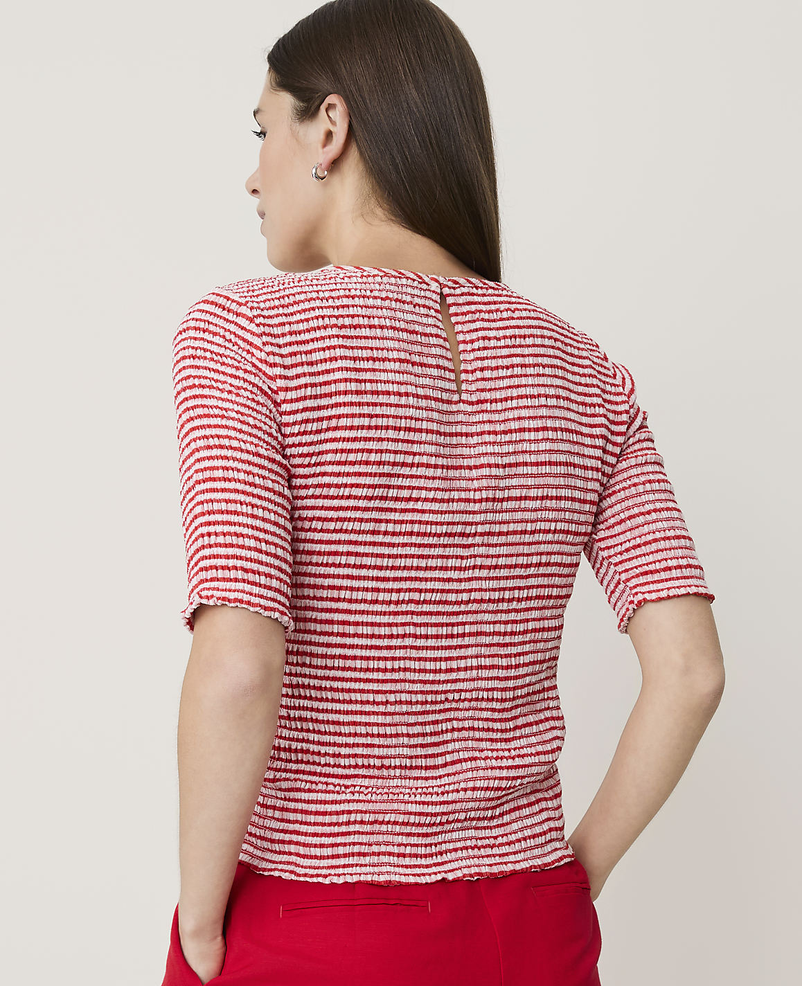 A woman in a red and white striped top and red pants stands against a plain white background.