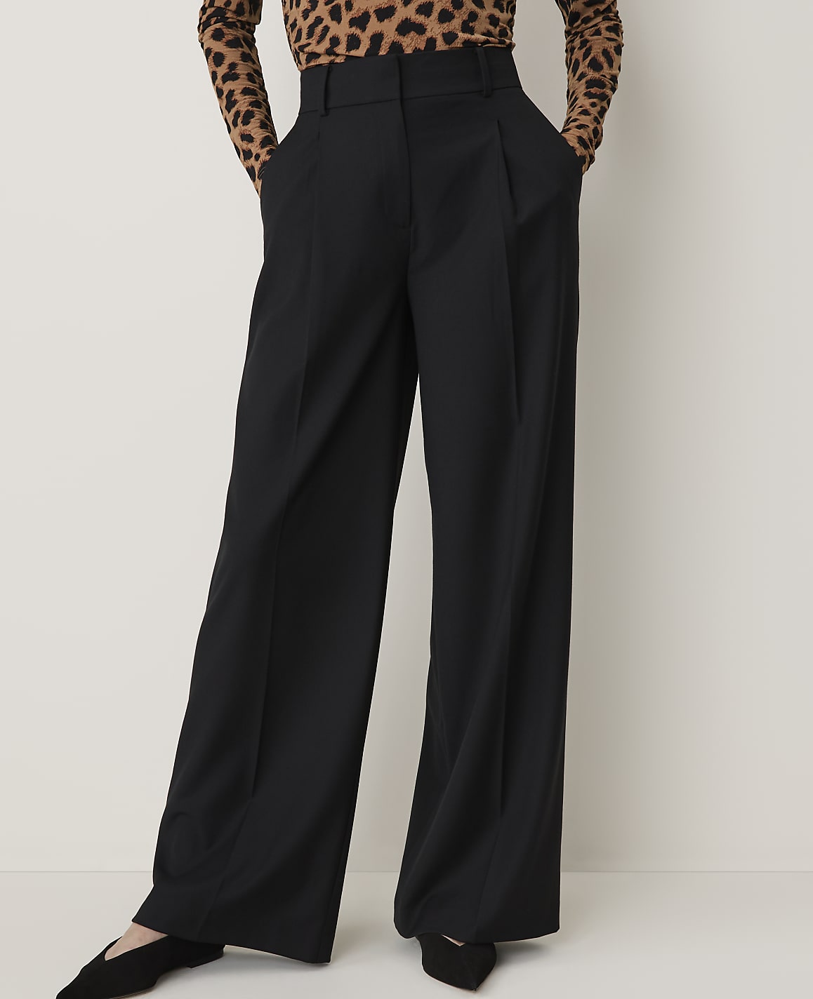 A person wearing black wide-leg pants and a leopard-print top stands against a plain white background.