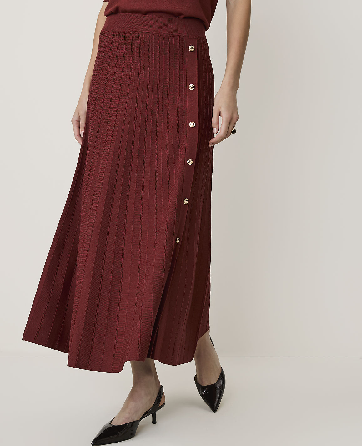 A woman in a maroon knit skirt and black heels stands against a plain white background.