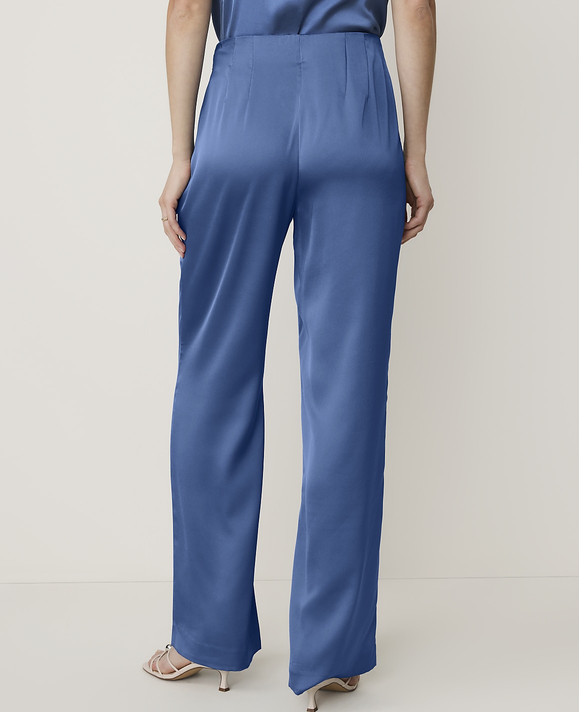 A person wearing blue satin wide-leg pants stands against a plain, light-colored background.