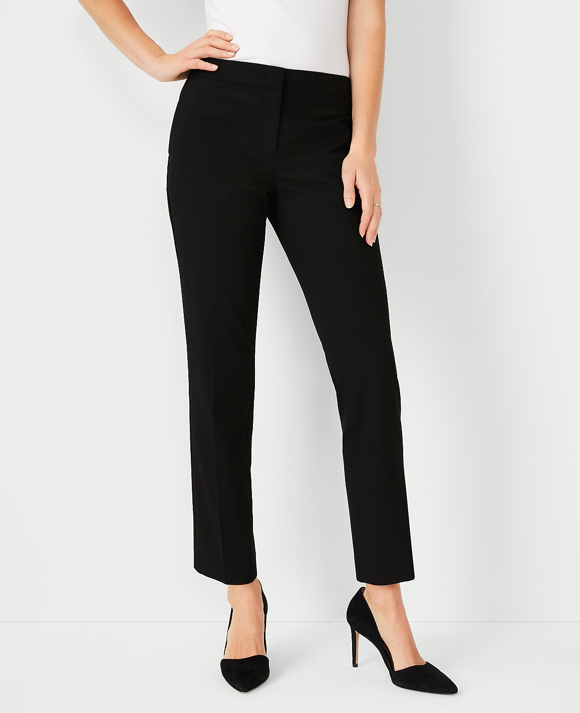 A woman in black pants and heels stands against a plain white background.