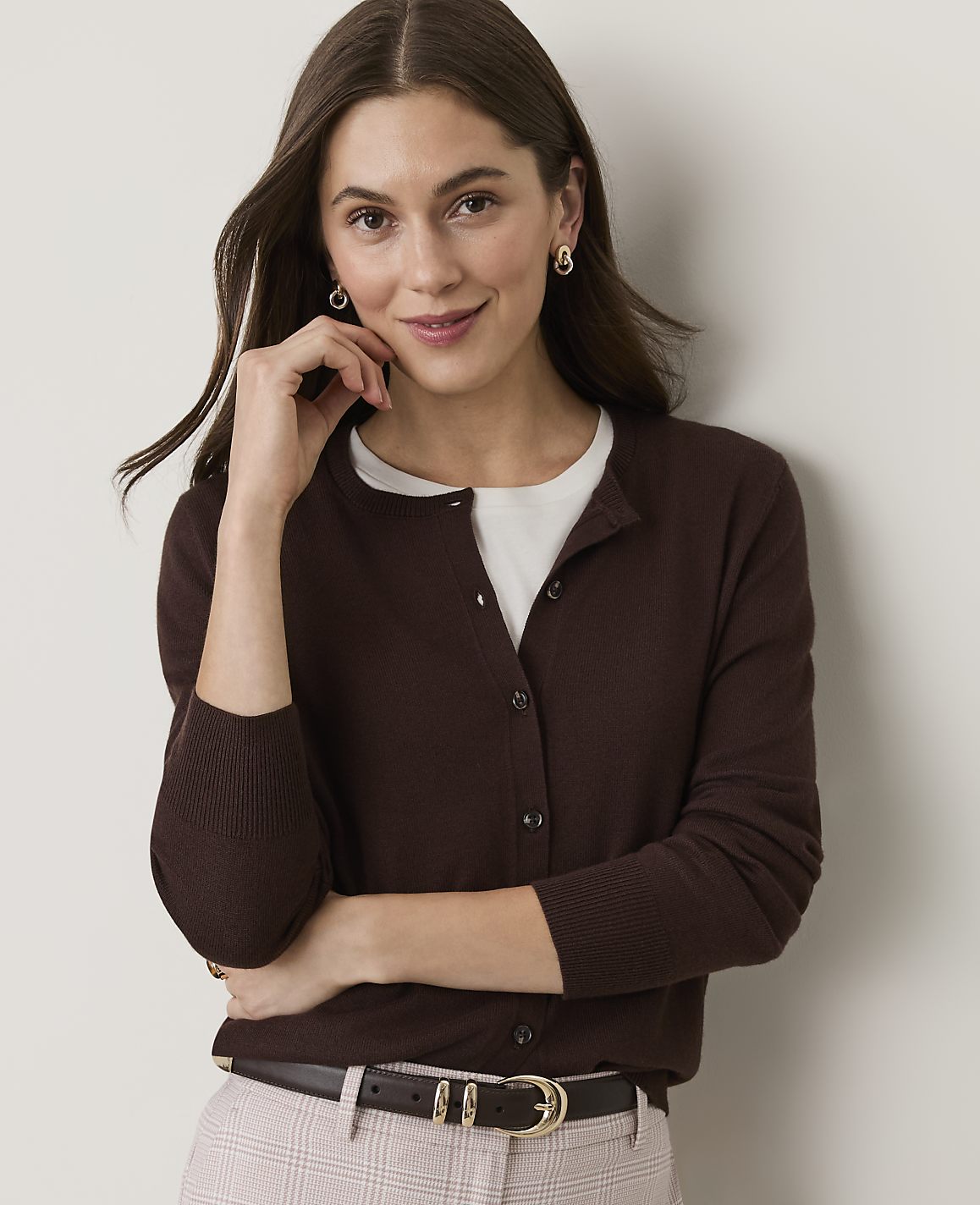 A woman in a brown cardigan and white shirt smiles gently against a plain, light-colored background.
