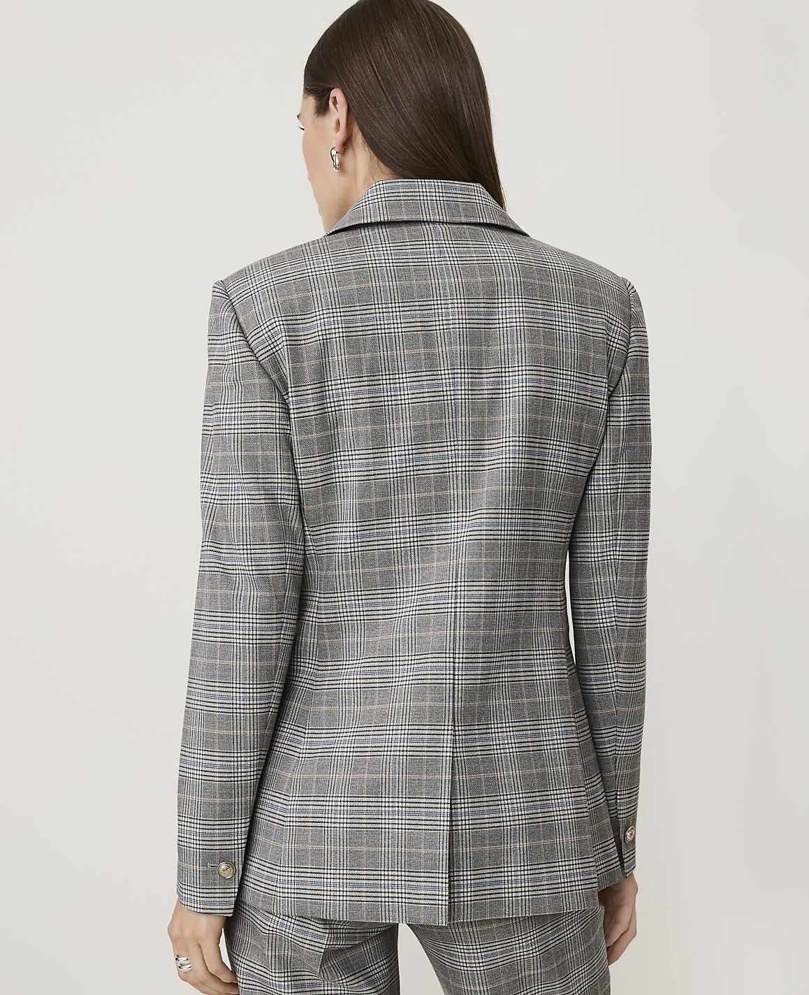 A woman in a grey plaid blazer and pants stands against a plain white background.