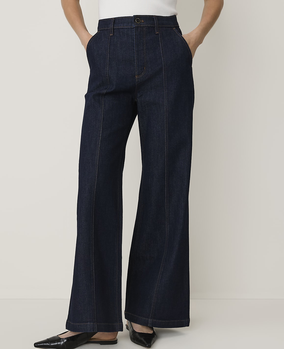 Dark wash flared jeans with a white top and black pointed-toe flats are displayed against a plain white background.