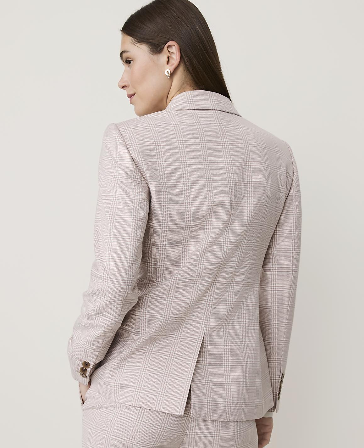 A woman in a light-colored plaid blazer and matching pants stands against a plain, light background.