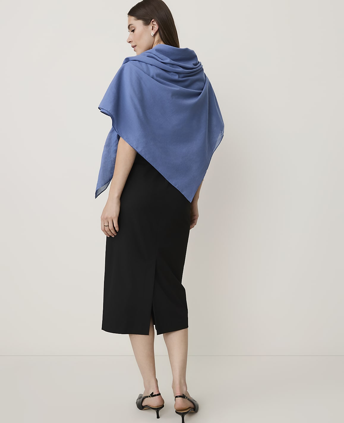 A woman in a black skirt and blue shawl stands against a plain white background.