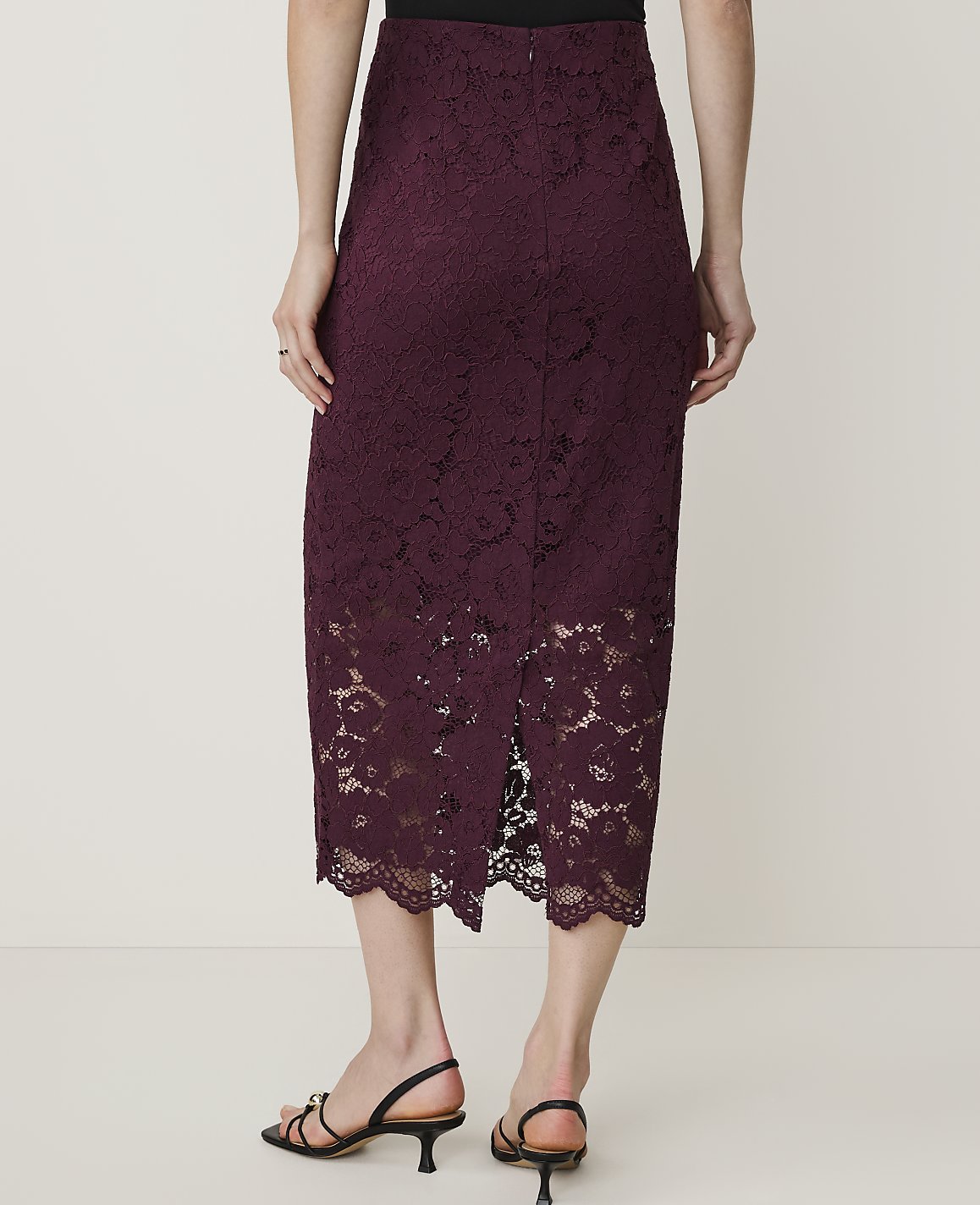 A woman in a burgundy lace skirt and black sandals stands against a plain white background.