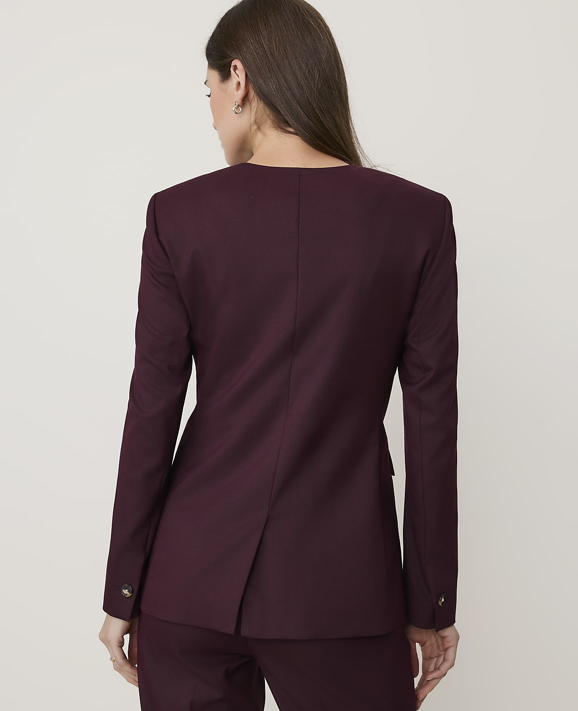 A woman in a burgundy blazer and pants stands against a plain white background.