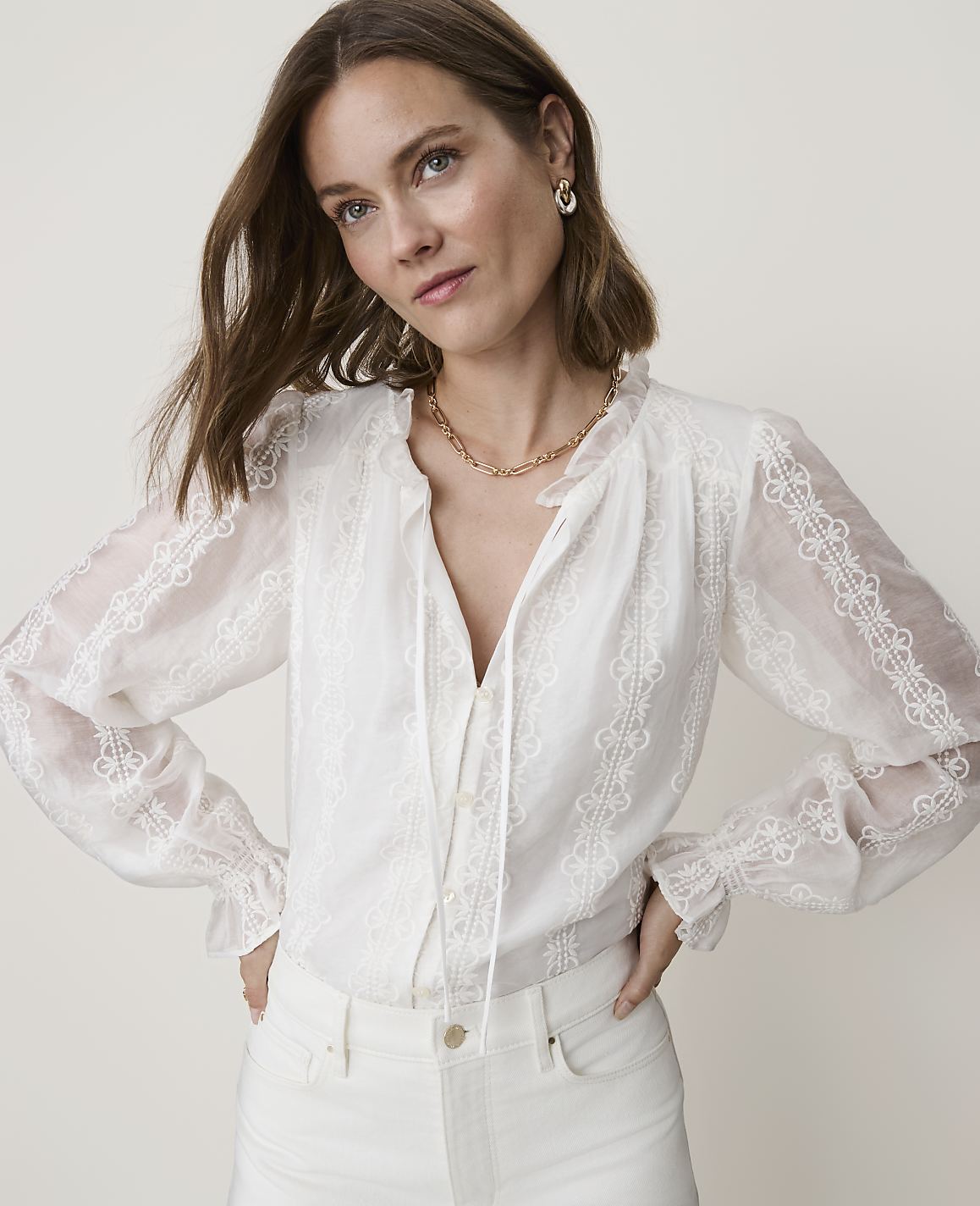 A woman in a white lace blouse and white jeans poses against a plain white background.