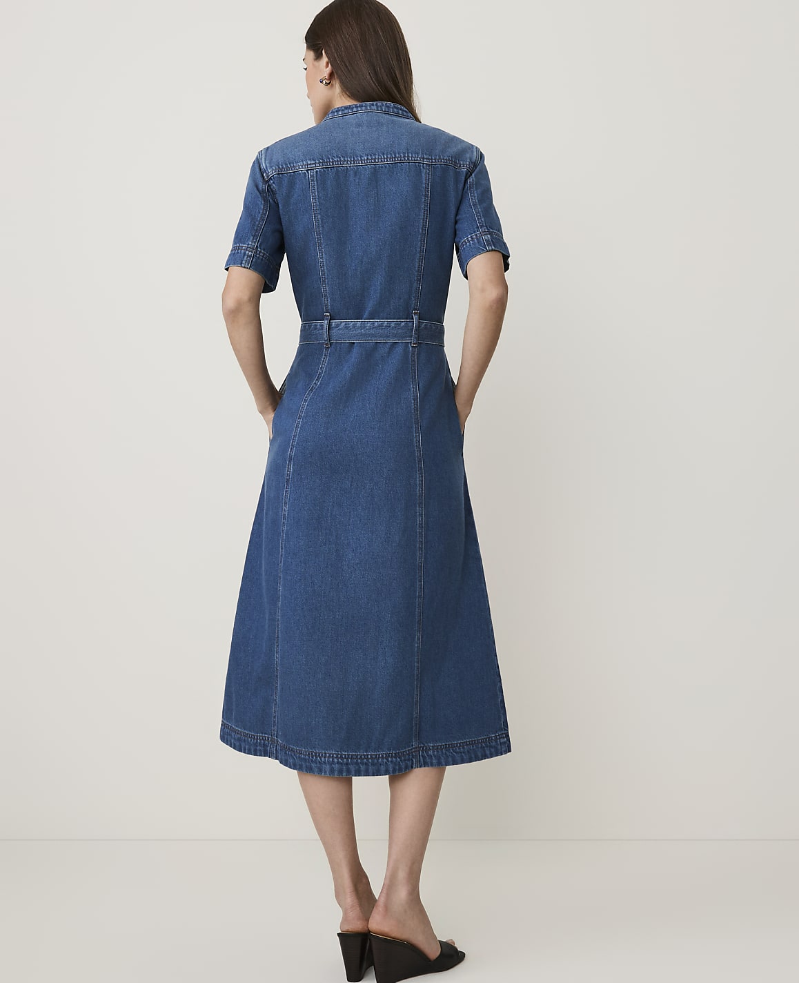 A woman in a denim dress stands against a plain, light-colored background.