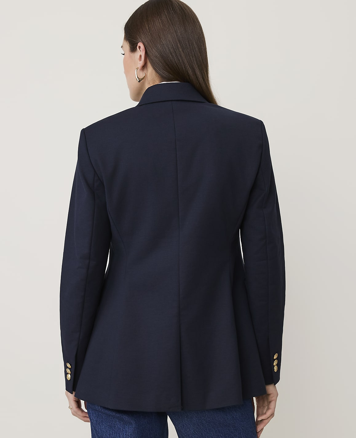 A woman in a navy blazer with gold buttons stands against a plain, light-colored background.