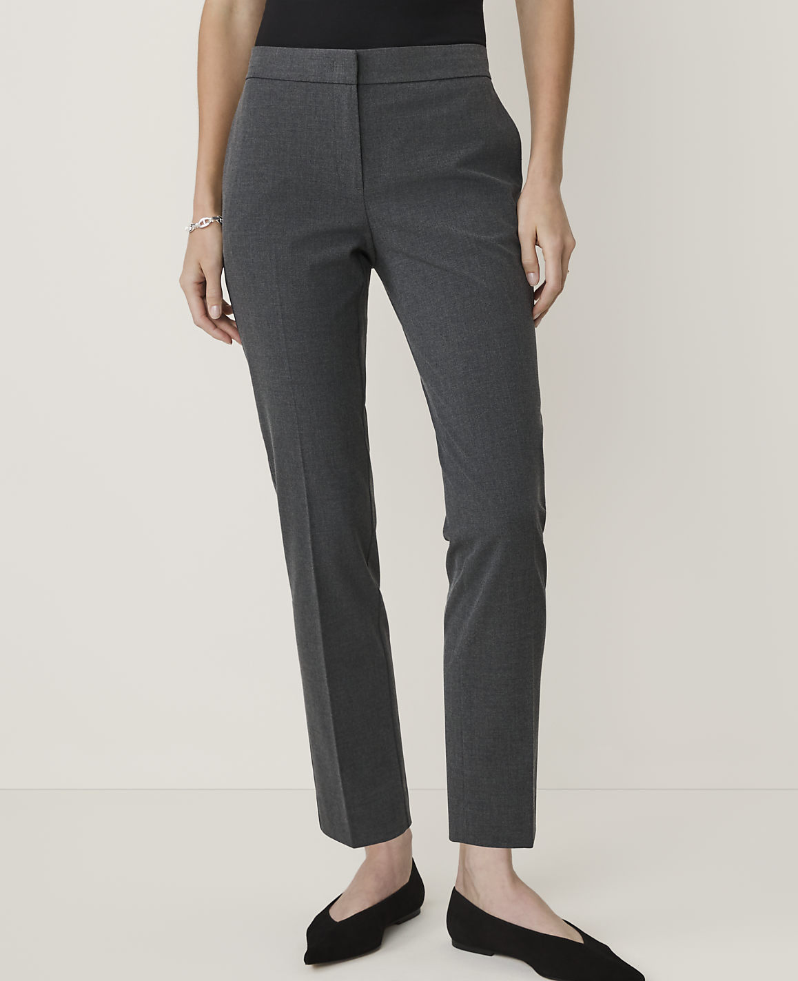 A person stands in dark grey pants and black flats against a plain, light grey background.