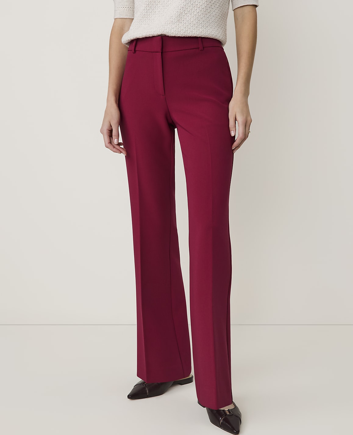 A person in burgundy flared trousers and a cream-colored top stands against a plain white background.