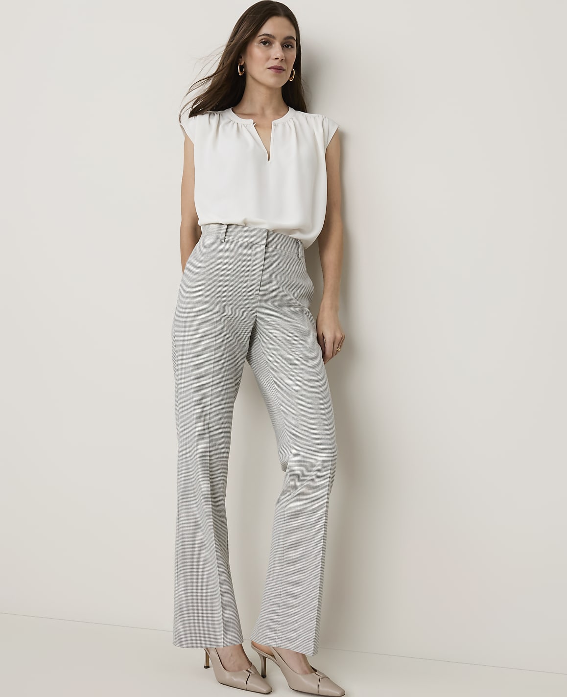 A woman in a white blouse and checkered pants stands against a plain white background.
