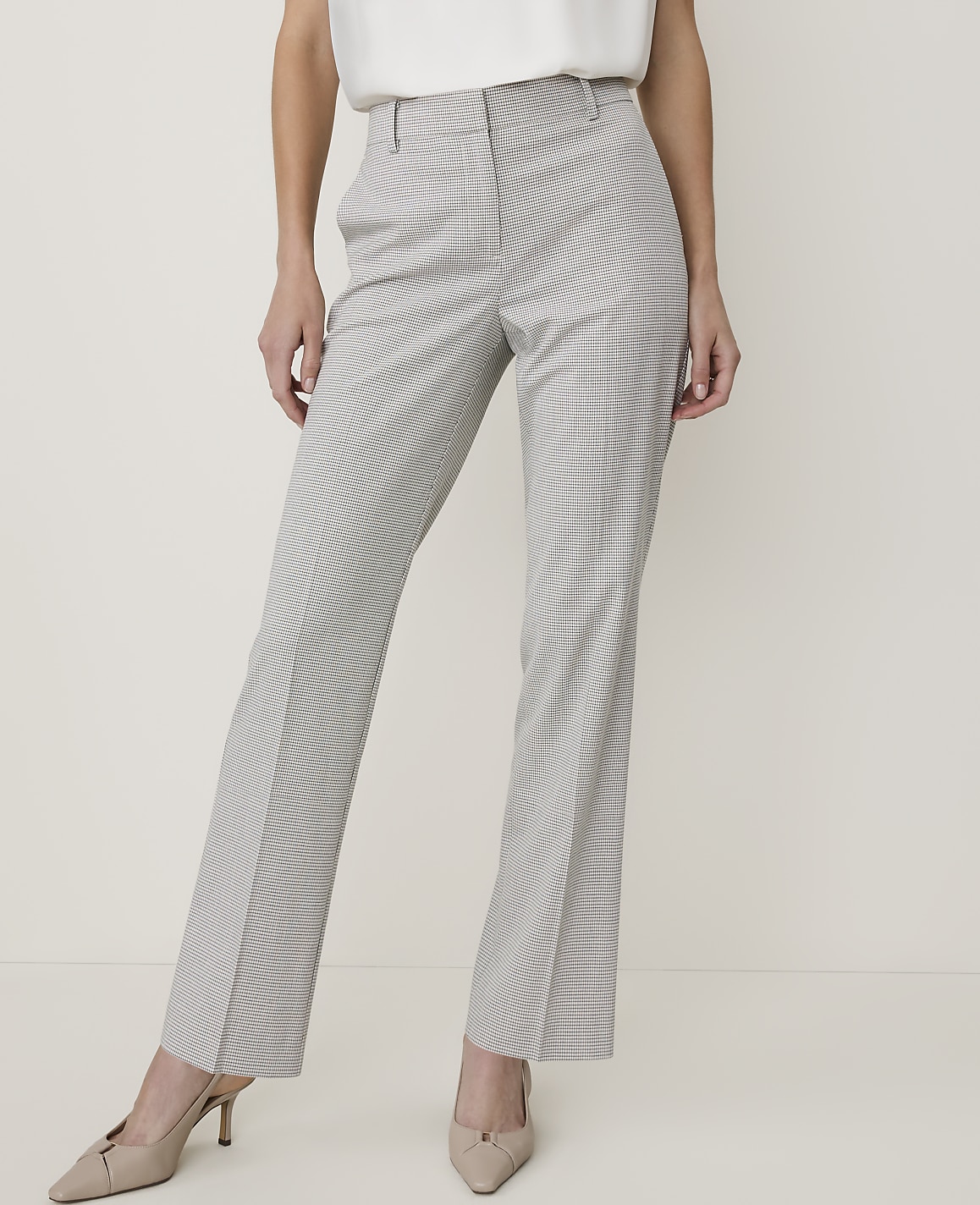A woman in pinstripe pants and heels stands against a plain, light-colored background.